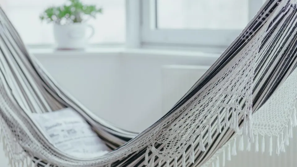 Helle Boho-Hängematte mit Fransen vor einem Fenster mit Zimmerpflanze